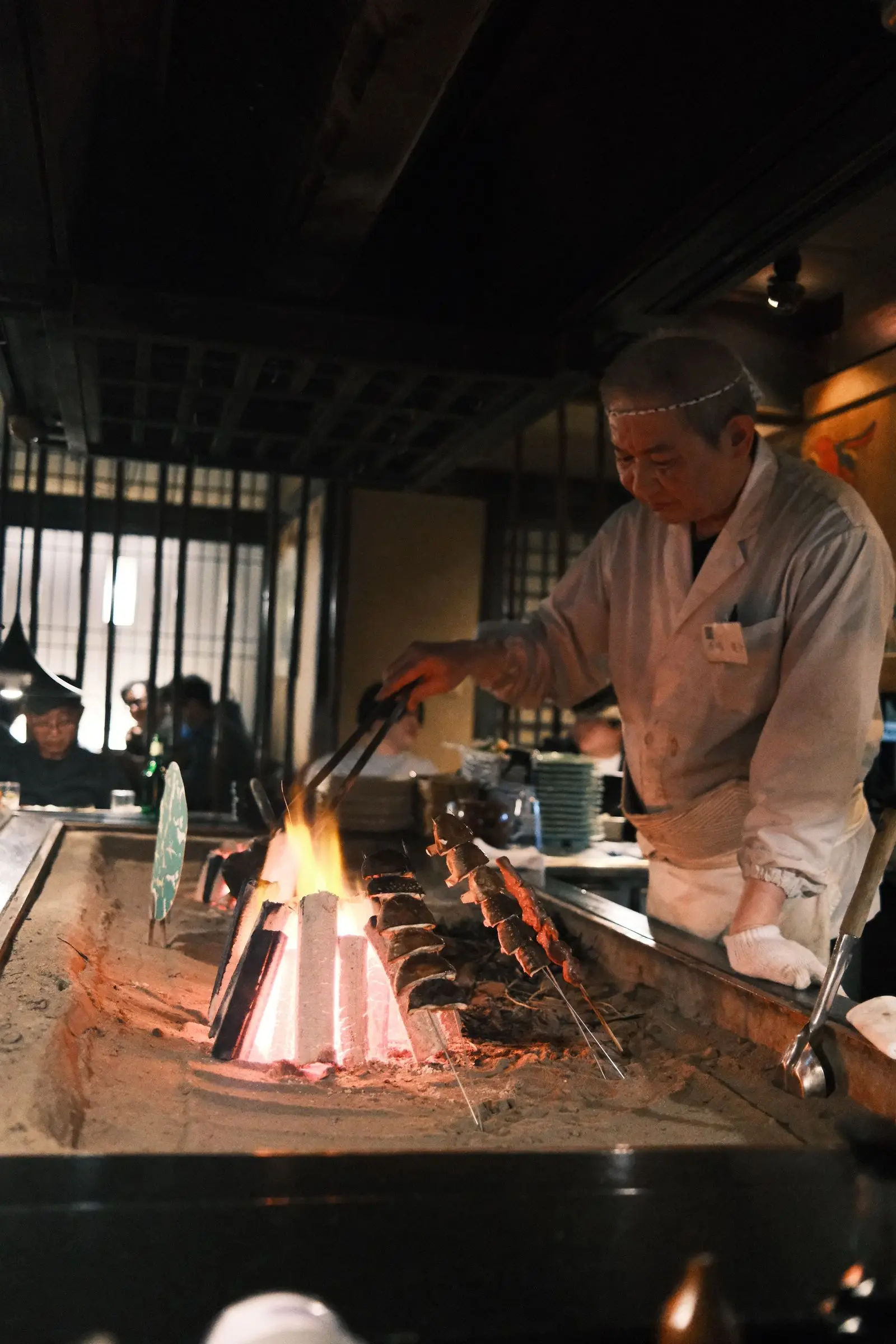 A cook's hands turning skewers over binchotan flames